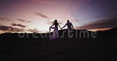 日落时分的浪漫时光对于一对年轻夫妇来说，他们享受着一起走过布满沙石的田野的时光